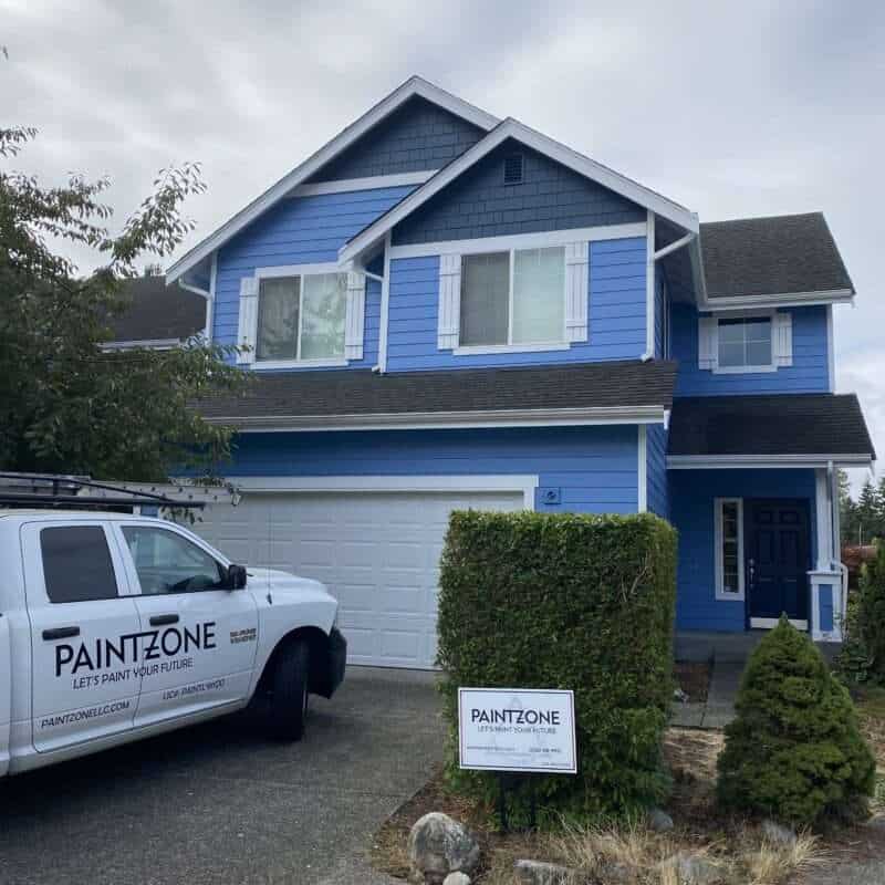 Image displays the charming exterior of a Queen Anne style home, painted in a delicate light blue hue. Highlighting its architectural details are navy blue accent shingles that add depth and character to the structure. The navy blue contrasts brilliantly with the main color, enhancing the building's vintage charm. White trims outline the windows and doors, providing a crisp contrast that frames the home's features. This combination of colors brings a fresh, yet traditional appeal to the home, reflecting the elegance of Queen Anne style.
